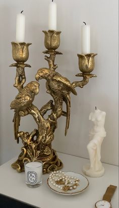 a gold candelabra with three candles on top of it next to a figurine