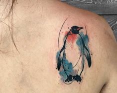 a watercolor penguin tattoo on the back of a woman's shoulder