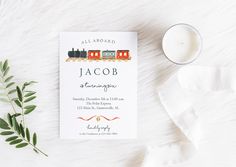 a wedding card with a train on it next to a candle and some greenery