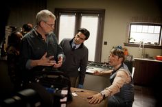 three men in a kitchen talking to each other while one man holds his hand out