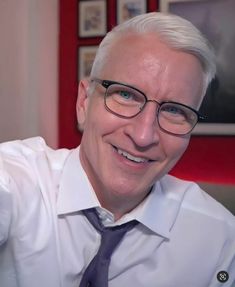 a man wearing glasses and a tie smiling at the camera with his hand on his hip