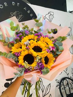 a bouquet of sunflowers is being held up by someone's hand in front of a wall