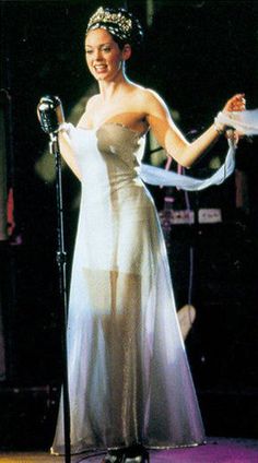 a woman in a white dress standing next to a microphone and wearing a tiara