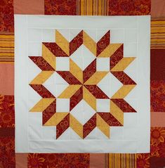 a quilted wall hanging with an orange and yellow star design on the center piece