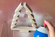 a hand holding a spray bottle near a piece of wood that is shaped like a triangle