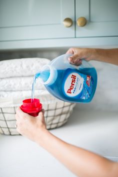 a person is pouring water into a red cup on a white counter top with towels in the background