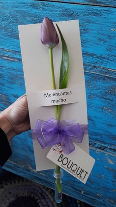 a hand holding a card with a purple tulip on it that says me encantas mucho