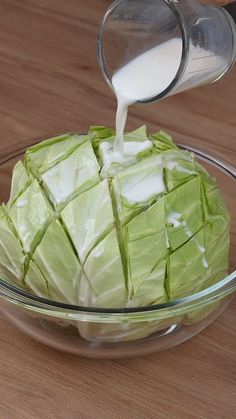 a person pouring milk into a bowl filled with lettuce and cubed cheese