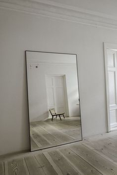 a mirror sitting on top of a wooden floor next to a white wall and door