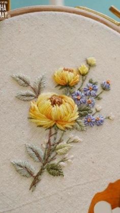 a close up of a embroidery on a hoop with yellow flowers and bluebells