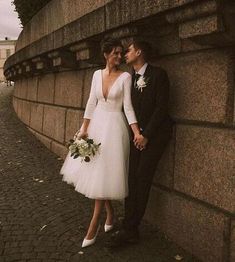 a bride and groom leaning against a stone wall