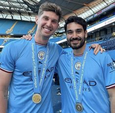 two men standing next to each other in front of a soccer stadium holding up medals