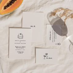 the wedding stationery is laid out on top of white paper with a slice of papaya