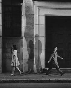 a man and woman walking down the street in front of an open door with shadows on it