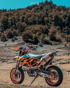 an orange and black dirt bike parked on top of a grass covered field with trees in the background