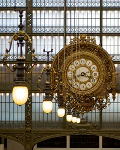 an ornate clock hanging from the ceiling in a train station with chandeliers and lights