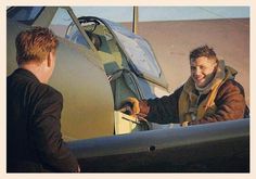 a man standing in front of an airplane talking to another man with his hand on the door handle