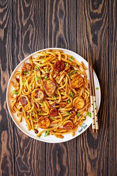 a white plate topped with noodles and meat next to chopsticks on top of a wooden table