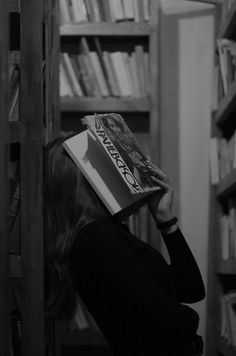 a woman reading a book in front of a bookshelf