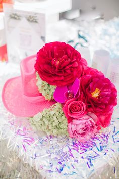 a pink hat with flowers on it sitting on top of a table next to other items