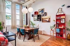 a dining room table with blue chairs and red bookshelves in front of a window