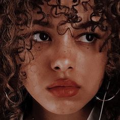 a close up of a person with curly hair and scissors in their hands, looking at the camera