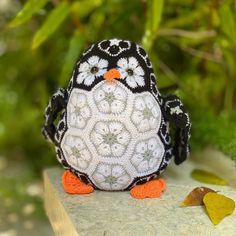 a small black and white penguin with flowers on it's head sitting on a rock