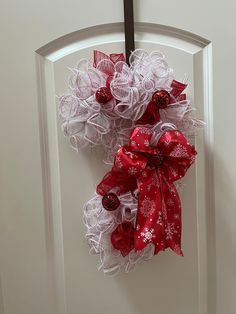 a red and white christmas wreath hanging on a door with ribbon attached to the front