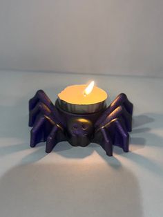 a purple candle holder with a lit candle in it on a white tablecloth background