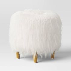 a white foot stool with wooden legs and fluffy fur on the top, in front of a gray background