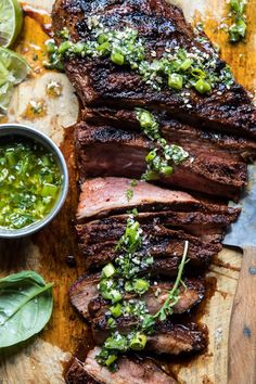 sliced steak with green sauce and garnish on wooden cutting board