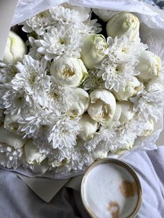 a bouquet of white flowers next to a cup of coffee