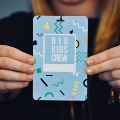 a woman holding up a small card with the words big kids crew on it in front of her face