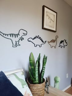 three dinosaur wall decals on the wall above a bed with a plant in a basket