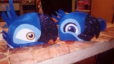 two blue birds sitting on top of a counter next to each other with eyes painted on them