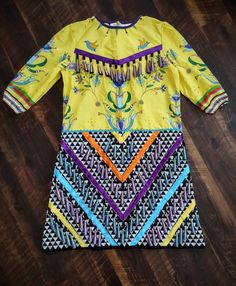 Woman's 100% cotton jingle dress.  Top fabric is a bright yellow floral fabric from Teton Trade Cloth. Bottom is a funky geometric black and white design. This dress holds 186 Teton Trade Cloth purple and blue ombre jingles and has a 20 inch zipper on the back. No inside lining but there is a collar lining. Purple, ocean blue, yellow, and satin ribbons holds the jingles. Dimensions: Chest: 48" Waist: 49" Hips: 49" Length: 44" Shoulder width: 5" Shoulder to shoulder: 23" Neck diameter: 18" Sleeve length: 20" Arm opening: 21.5" Size: 14-16 Material: 100% Cotton If you need additional measurements, please message me. Ahéhee' (Thank you) for browsing our store! Multicolor Cotton Dress With Graphic Print, Multicolor Graphic Print Cotton Dress, Patterned Cotton Dress With Graphic Print, Yellow Floral Print Dress For Festival, Cotton Graphic Print Patterned Dresses, Yellow Cotton Festival Dress, Yellow Cotton Dress For Festival, Fitted Yellow Dress With Graphic Print, Multicolor Cotton Ikat Print Dress