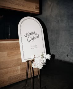 a sign with flowers on it sitting in front of a wooden wall and wood floor