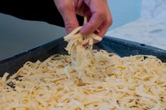 a person is sprinkling cheese on top of noodles in a pan with a spatula