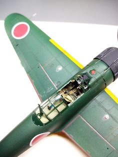 an old model green airplane with red and yellow stripes on it's sides, sitting on a white surface