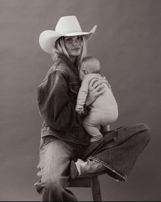 a woman sitting on top of a chair holding a baby in her arms and wearing a cowboy hat