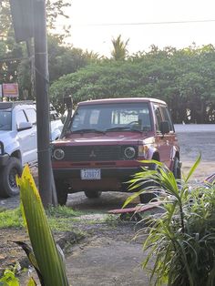 a red car parked on the side of a road next to a tree and bushes