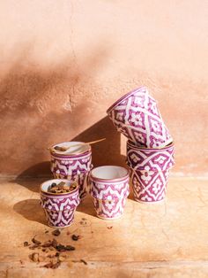 purple and white patterned cups sitting on top of a wooden table next to a wall