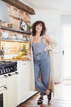 a woman standing in the kitchen with her arms behind her back and smiling at the camera