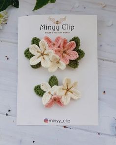 three crocheted flower clips in pink, white and green on top of a card