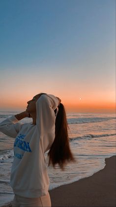 a woman standing on top of a sandy beach next to the ocean at sun set