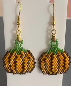 a pair of beaded pumpkins are hanging from earwires on a hook