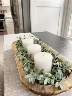 three candles sitting on top of a wooden tray filled with greenery and eucalyptus leaves