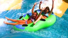 two girls are riding on an inflatable raft down the water slide at a theme park