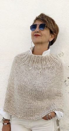 a woman in white pants and a sweater with blue sunglasses on her head is leaning against a wall