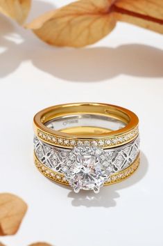 two gold and white wedding bands with a diamond ring in the middle, surrounded by leaves